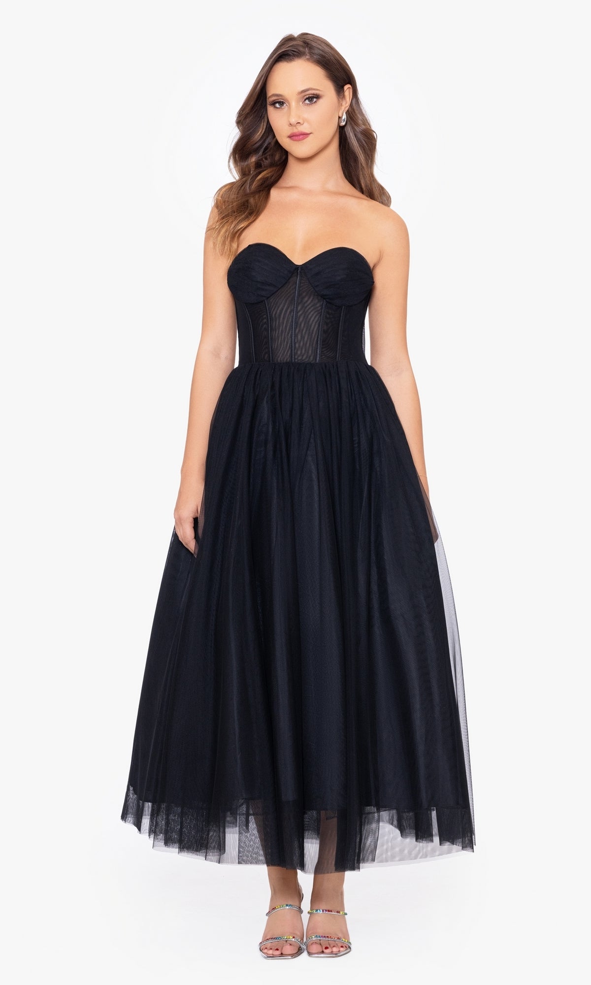 A woman models the Black Strapless Tea Length Wedding-Guest Dress, featuring a fitted corset bodice and sheer mesh details, against a plain white background—an ideal choice for an elegant wedding guest look.